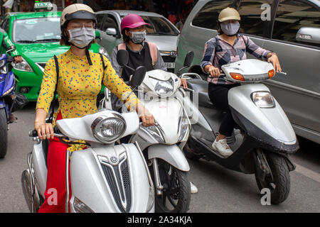 Trois jeunes femmes avec masque de pollution sur les motos dans la rue de Hanoi, au Vietnam. La pollution est un problème énorme en asie du Sud-est. Banque D'Images