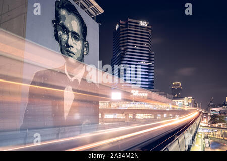 L'exposition à long shot de train BTS en passant par la fin de portrait géant le roi Bhumibol sur mur de la rue la nuit à Bangkok Banque D'Images