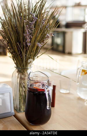 Maison d'été limonade rouge foncé avec des tranches de citrons dans un pot sur la table en bois. Fleurs séchées bouquet arrière-plan. Journée ensoleillée arrière-plan flou Banque D'Images