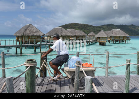 Un hôtel travailleur est vu rouler à bicyclette à un aqua-centric.Luxury Resort Bora Bora est une île volcanique de la Polynésie française, dans l'océan Pacifique. C'est Tahiti et l'île la plus célèbre d'une destination touristique internationale importante célèbre pour ses stations balnéaires de luxe. La population est d'environ 9 000 habitants. Banque D'Images