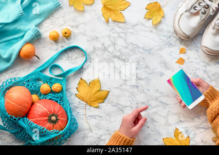 Femmes avec un téléphone mobile, les citrouilles en prise ou chaîne sac, chaussures blanc, pull bleu et jaune des feuilles. Autumntime mise à plat, vue supérieure avec copier- Banque D'Images