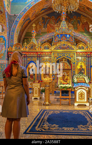 Krasnoyarsk, Russie, 15 septembre 2019 : une femme dans un foulard de prier dans une église orthodoxe en face de la sainte icône. L'intérieur de l'Église russe traditionnelle Banque D'Images