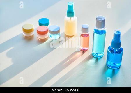 Divers articles de toilette dans des bouteilles en plastique clair voyageant sur fond de papier neutre avec de longues ombres, copie-space Banque D'Images