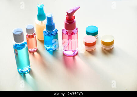 Divers articles de toilette dans des bouteilles en plastique clair voyageant sur fond de papier neutre avec de longues ombres, copie-space Banque D'Images