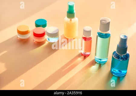 Divers articles de toilette dans des bouteilles en plastique clair voyageant sur fond de papier neutre avec de longues ombres, copie-space Banque D'Images