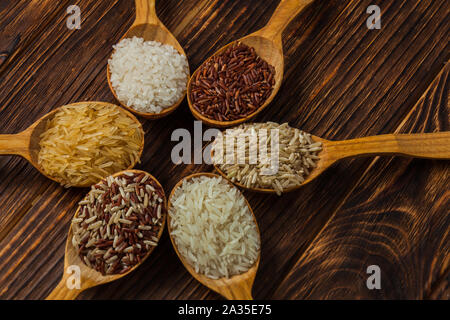 Cuillères en bois avec différents types de riz sur le fond en bois Banque D'Images