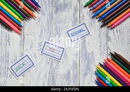 Concept créatif avec les fournitures scolaires. Les étiquettes avec texte retour à l'école et des marqueurs sur un bureau en bois. Banque D'Images