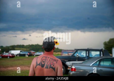 08182019 - Bethel, New York, USA : un homme avec un tatouage de l'orthographe, 'Amour', et une fleur dans ses cheveux ressemble à un orage sévère venant en sens inverse sur la dernière journée au cours de la réunion de la route Yasgur Max Yasgur's farm à pendant les célébrations du 50e anniversaire de Woodstock, dimanche, Août 18, 2019 près de Bethel, New York. Organisateur de Woodstock Michael Lang, l'événement a été annulé mais anniversaire les activités ont continué au Arrowhead Ranch, Bethel Woods (le site de l'original Woodstock en 1969), Hector's Inn, et Yasgur's Farm. Banque D'Images