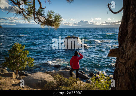 Tahoe City, Californie / Etats-Unis : 27 sept 2019: Une touriste féminine en manteau rouge regarde sur le lac Tahoe par une journée ensoleillée. Banque D'Images