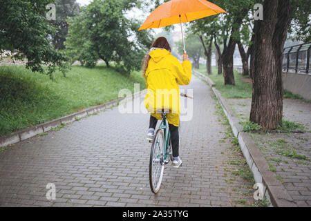 Balade à vélo sous la pluie. Femme en imperméable riding bicycle et holding umbrella Banque D'Images