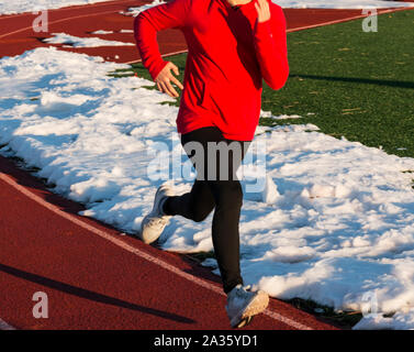 Une voie secondaire runner sprint sur une piste qui a eu la neige à la pelle au loin de elle sur un bel après-midi ensoleillé à la pratique. Banque D'Images