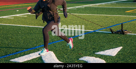 Une voie secondaire sprinter est tirant un traîneau avec des poids sur elle à travers un champ de gazon vert en hiver. Banque D'Images