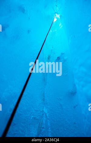 Jusqu'à la corde pour une entrée étroite dans une grotte de glace sur le glacier du saumon au Canada. Entouré par de beaux bleu clair à l'intérieur de la caverne de glace. Banque D'Images
