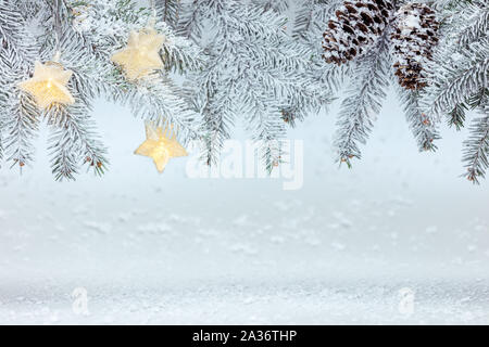 Branches de sapins avec les cônes sous la neige avec star garland feux arrière-plan de la nouvelle année. Banque D'Images