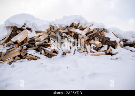 Une pile de bois de chauffage coupé se trouve dans la neige parmi les amoncellements de neige, contre le ciel et les nuages, sur un jour d'hiver glacial. Banque D'Images