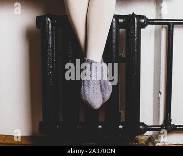 La fille est assise sur le rebord et se réchauffe les jambes en laine tricoté à Chaussettes Chaussettes le radiateur, par une froide soirée d'hiver. Banque D'Images