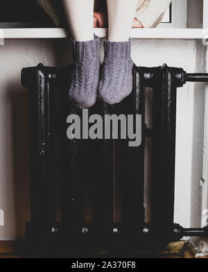 Une fille est assise sur un rebord de mettre leurs pieds dans des chaussettes en laine tricotées sur le radiateur et chauffée par une froide soirée d'hiver. Banque D'Images