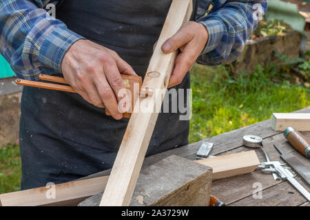 Un vieux menuisier travaillant avec du bois à l'extérieur durant une journée d'été Banque D'Images