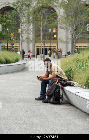 Un homme assis en chiffon occasionnel vérifie son téléphone à la Cleveland Place publique donnant sur le centre-ville de tour. Cleveland, Ohio, USA. Banque D'Images