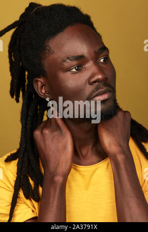 Modèle masculin attentionné pensive avec nouvelle coiffure de toucher son cou à la recherche de côté, la photo en gros fond jaune isolé. Banque D'Images