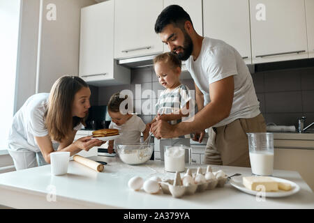 Petite fille qui sent chaud délicieux pancakes tandis que sœur aînée et son père mixer la pâte. la photo en gros plan. Banque D'Images