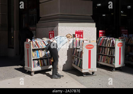 Une jeune femme parcourt les livres en vente à l'extérieur de la librairie Strand à Broadway dans Greenwich Village, Manhattan, New York. Banque D'Images