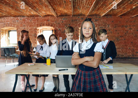 Jeune fille sérieuse avec bras croisés posant pour l'appareil photo pendant que ses amis travaillant au bureau Banque D'Images