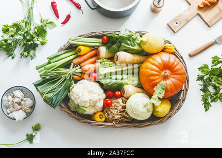 La récolte des légumes organiques divers pour cuisiner et manger savoureux dans le bac en bois blanc sur le bureau avec des ustensiles de cuisine les herbes et épices, vue d'en haut. Guérir Banque D'Images