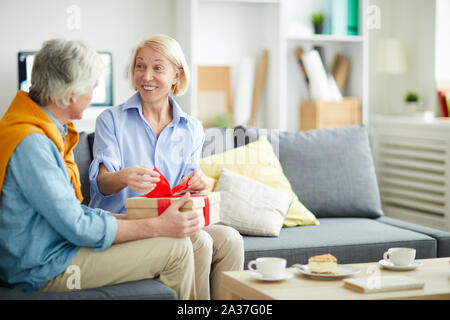 Portrait of senior woman opening gift excité de prendre soin mari assis sur un canapé confortable en intérieur, copy space Banque D'Images