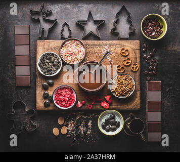 Noël fait maison Préparation de l'écorce de chocolat avec du chocolat fondu et différents topping chocolat cassé : tiges de bretzel, fruits secs, noix, caramel, l Banque D'Images