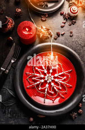 Table de dîner de Noël avec des plaques rouge et noir, décoré avec des flocons, de bougies et de guirlandes lumineuses sur fond sombre. Vue d'en haut Banque D'Images