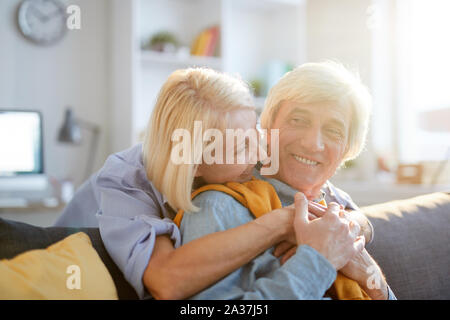 Portrait chaleureux de carefree senior couple embracing tendrement bénéficiant de temps libre à la maison éclairée par la lumière du soleil, copy space Banque D'Images