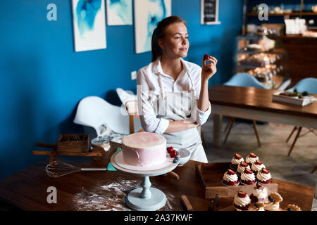 Jeune femme cuisinière avoir une pause dans la cuisine, dégustation berry dans la cuisine avec un mur bleu, temps libre, loisirs, passe-temps Banque D'Images