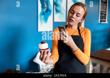 Black à chandail jaune , tablier noir holding smart phone, cupcake, photo,business Banque D'Images