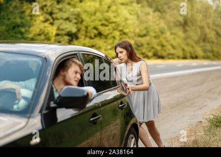 Jeune femme poussant broken voiture avec man on road Banque D'Images