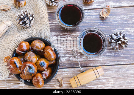 Châtaignes grillées savoureuses sur Bol en céramique servi avec deux des verres de vin rouge sur la table rustique en bois. Maison de vacances d'hiver fête traite l'arrière-plan. Vue d'en haut Banque D'Images