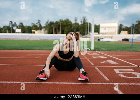 Fatigué female jogger assis sur le sol, le stade Banque D'Images