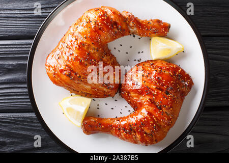 Partie de quart de poulet collant jambes avec des graines de sésame et citron gros plan sur une assiette. Haut horizontale Vue de dessus Banque D'Images