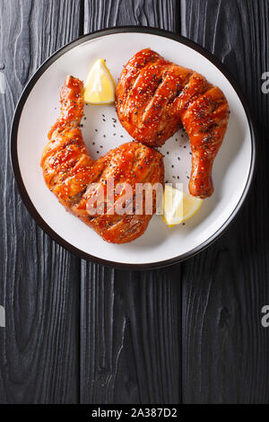 Sticky grillé savoureux les cuisses de poulet avec les graines de sésame et citron gros plan sur une assiette. Haut Vertical Vue de dessus Banque D'Images