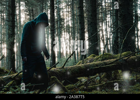 Une peur, l'horreur concept. Une silhouette encapuchonnée, fantasmagorique, à la recherche de la lumière rougeoyante flotter autour de sa tête et à travers une forêt de conifères en hiver. Banque D'Images