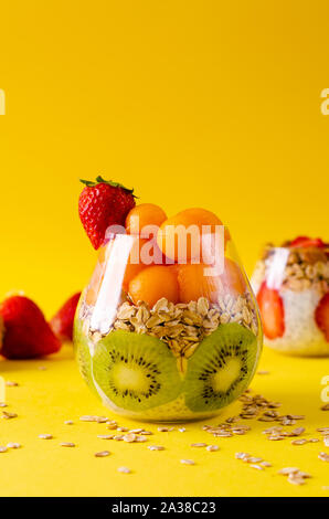 Chia pudding avec le kiwi, melon et oatmeals ou boules de papaye dans un verre sur fond jaune vif. Detox et sain petit-déjeuner superfoods concep Banque D'Images