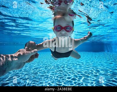 Fille nager sous l'eau dans une piscine avec l'aide de son père