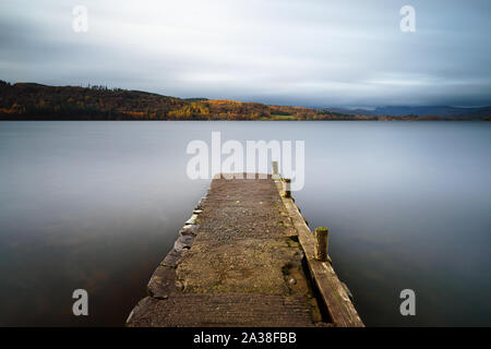 Une jetée en béton provient de la rive du terrain Miller sur le lac Windermere dans le Lake District sous un ciel couvert l'après-midi d'automne. Banque D'Images