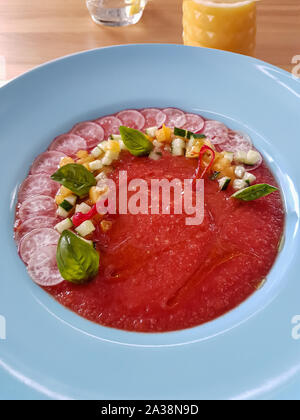 Restaurant espagnol servi gaspacho rafraîchissant potage de tomates rouges, servi en plaque blanche et décoré avec des légumes frais et basilic Banque D'Images