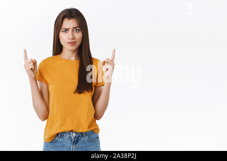 Sceptique, incertain et remise en question de bon à la brunette woman t-shirt jaune en soulevant un sourcil douteux, pointant vers le haut, comme regarder un peu l'appareil photo Banque D'Images