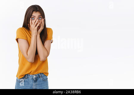 Peur, d'insécurité timide jeune fille brune, se cachant derrière les mains, doigts peeking through effrayé, tremblant de peur, regardant des films d'horreur Banque D'Images