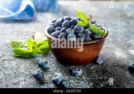 Les bleuets mûrs en ceramik bol avec menthe feuilles sur un fond de béton foncé Banque D'Images