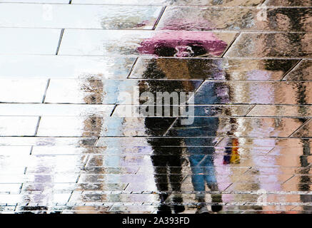 Réflexion floue ombre silhouette d'un couple en train de marcher ensemble sous le parapluie d'un caniche mouillé street dans la ville zone piétonne sur un jour de pluie Banque D'Images