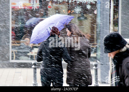 Belgrade, Serbie - 3 janvier 2019 : Deux jeunes femmes de traverser la rue en marchant sous le parapluie d'hiver enneigés jour dans la ville Banque D'Images