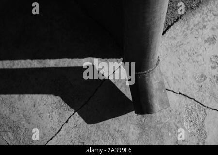 Échappement à l'angle de l'immeuble. Des fissures sur le sol de pierre. La lumière du soleil et l'ombre du tuyau de vidange. Photo en noir et blanc. Banque D'Images